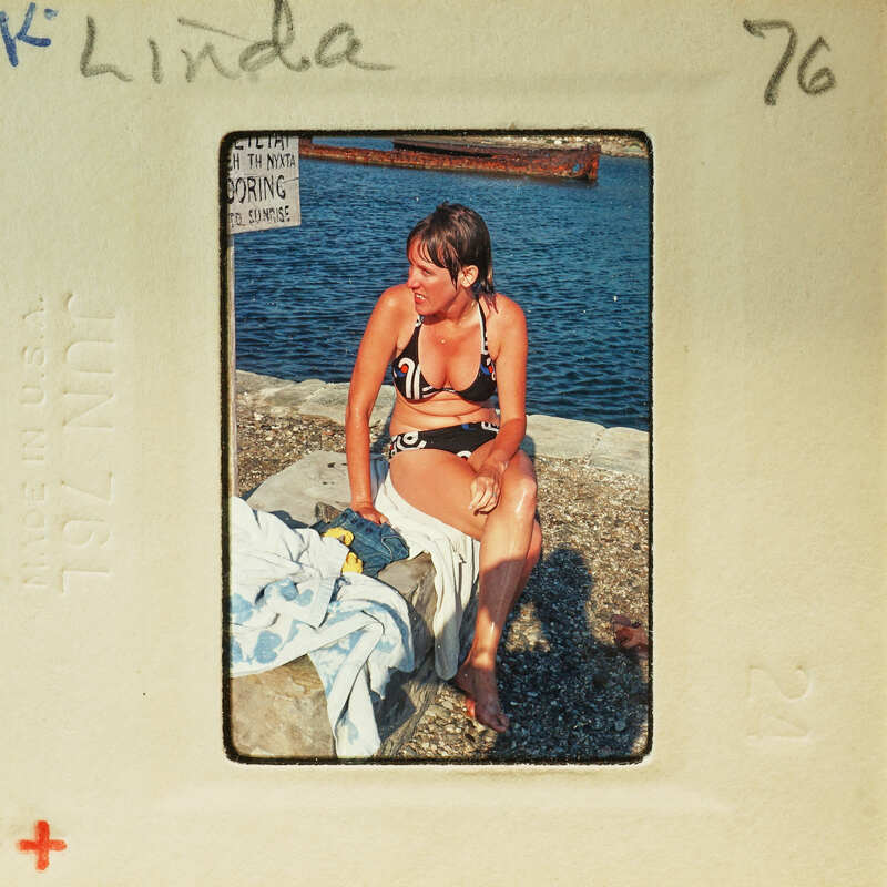 Woman sitting on a towel at the beach, wearing a bikini top and smiling.