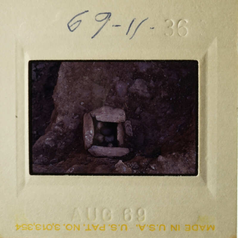 This is a photograph of an old slide showing a small cave entrance with rocks around it.