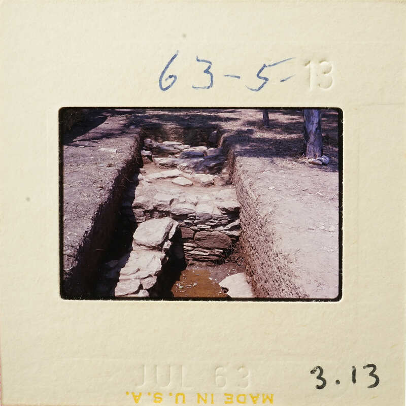 Stone-lined waterway with vegetation and trees in background.