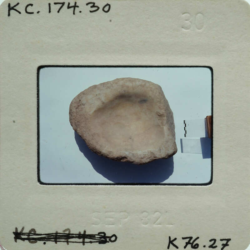 A photograph of a small, round, light-colored plaster fragment with a hole in the center.