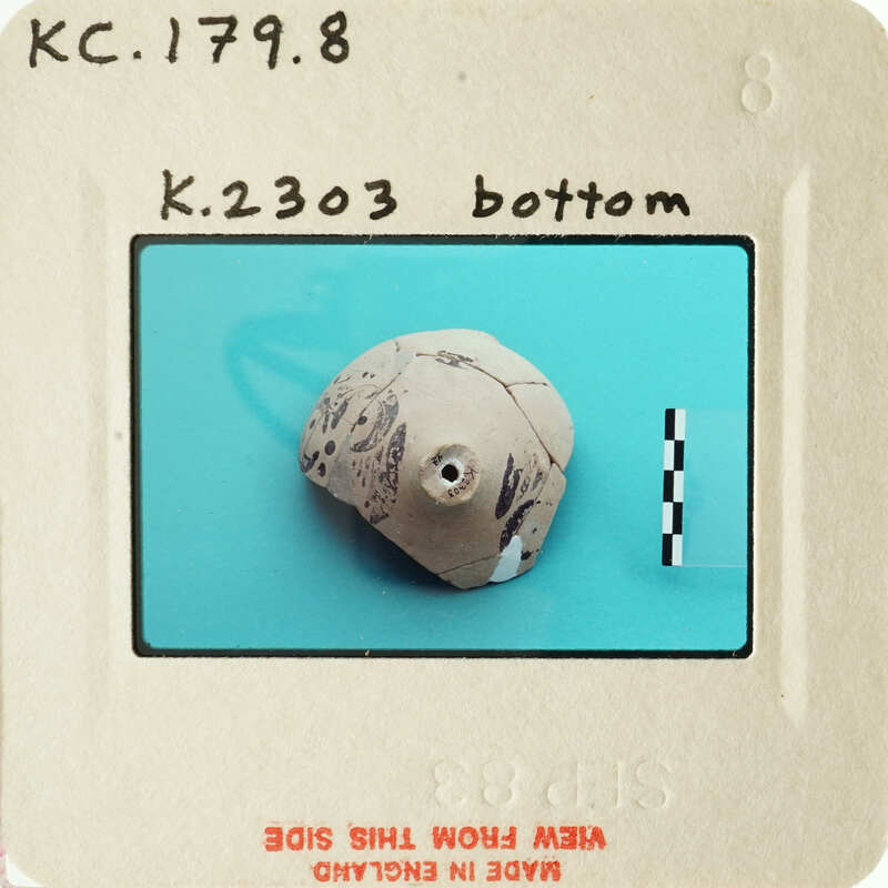 A small, round clay artifact with designs on a blue background.