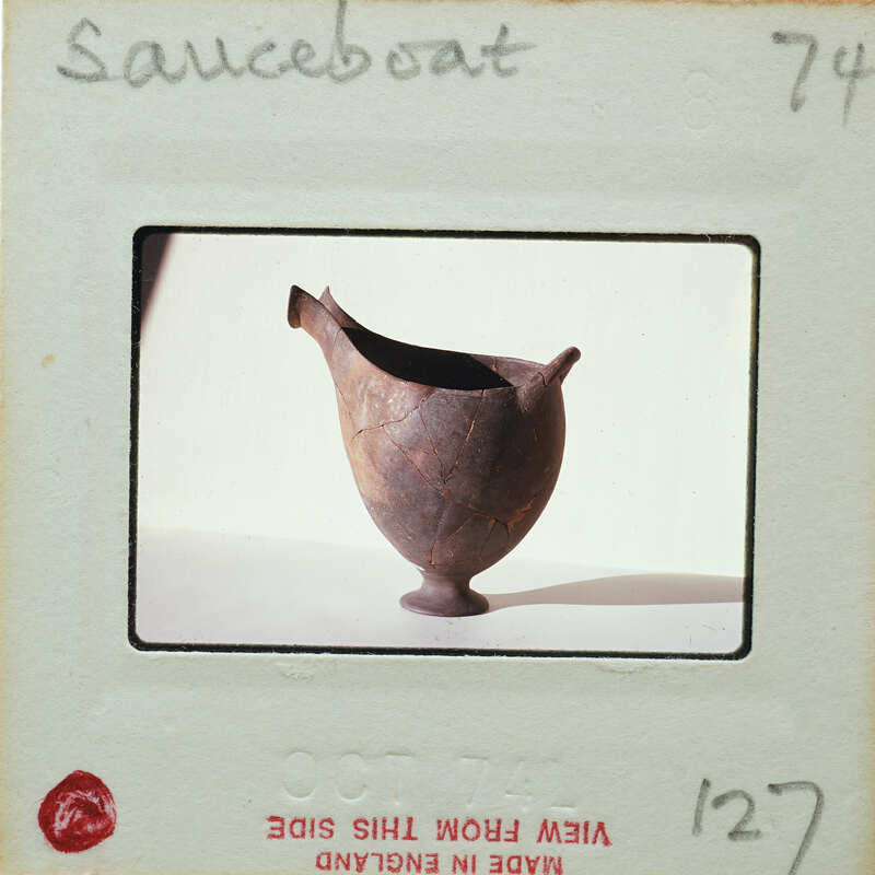 A small, dark brown clay pot with a handle and spout on a white surface.