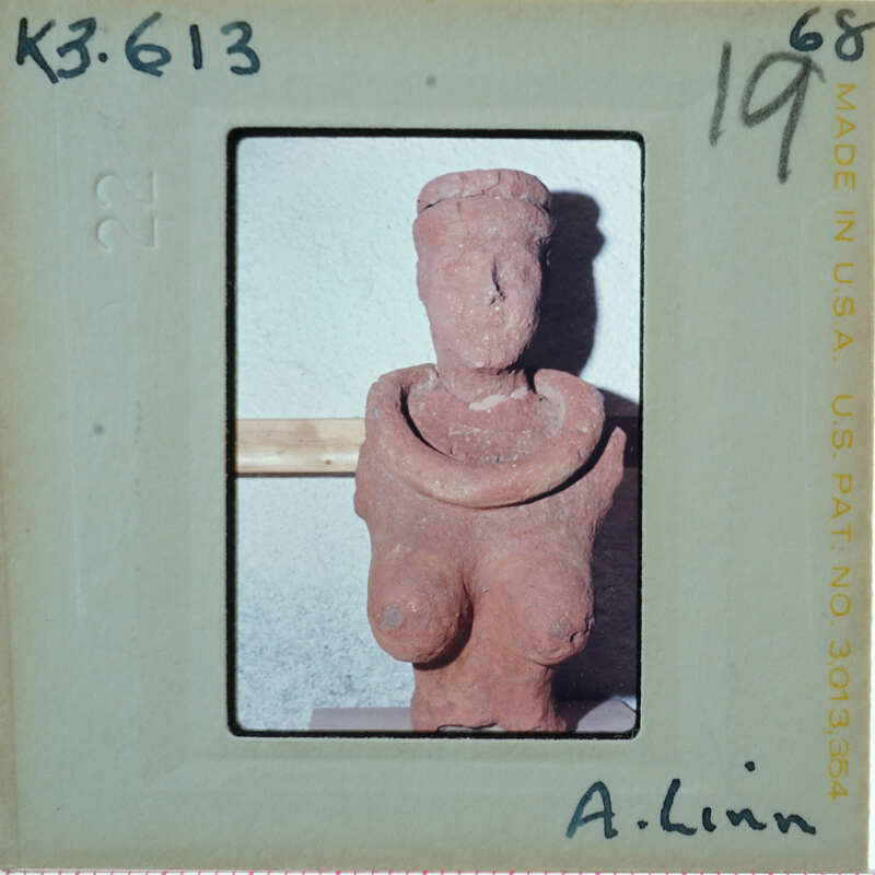 A clay figurine of a person with exaggerated breasts, on display in an indoor setting.