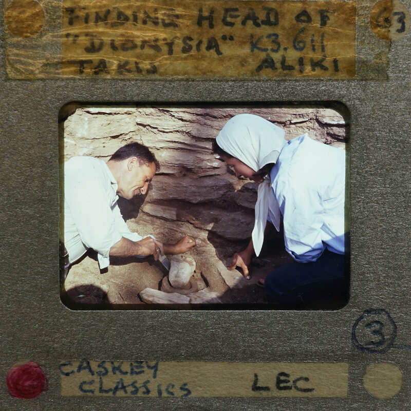 Two people examining a terracotta object (K3.611) at an archaeological site.