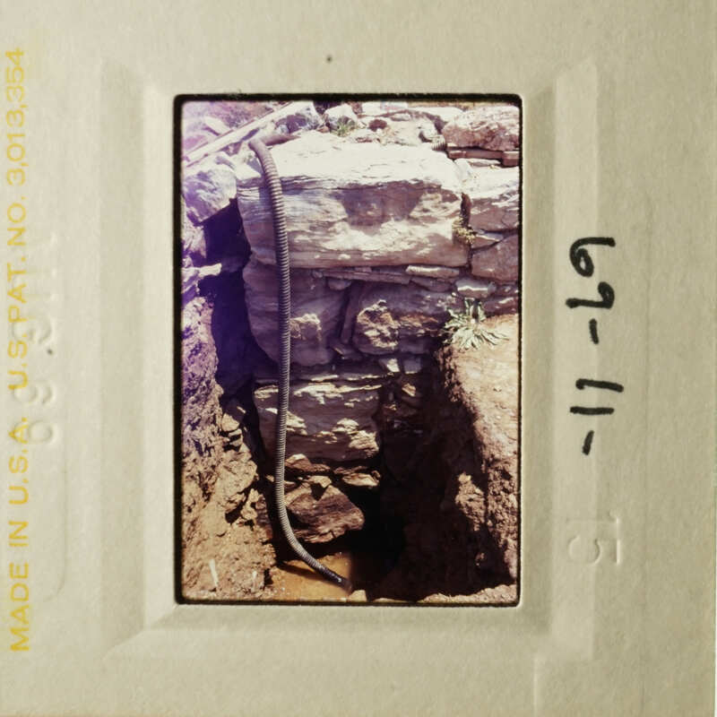 "An old photograph depicts an excavation site with a hose and rock wall."