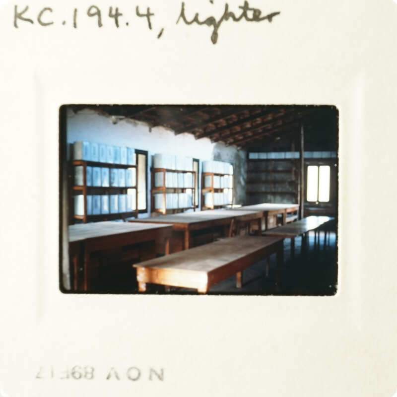 Photo of an empty library with long tables and shelves, taken from a low angle.