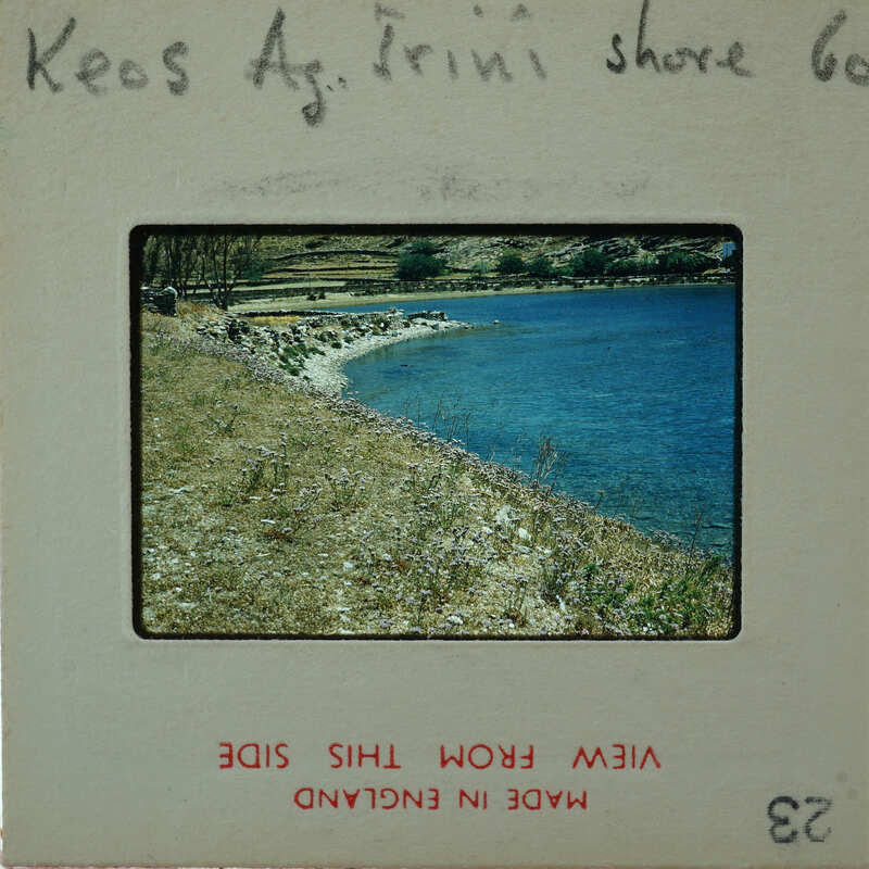 A vintage photograph of a serene beach scene with calm waters and a rocky shoreline, encased within an old film strip holder.