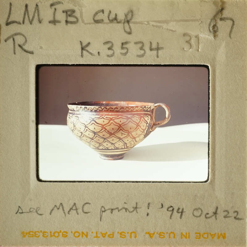 A photograph of an antique cup with intricate designs, displayed on a white surface.