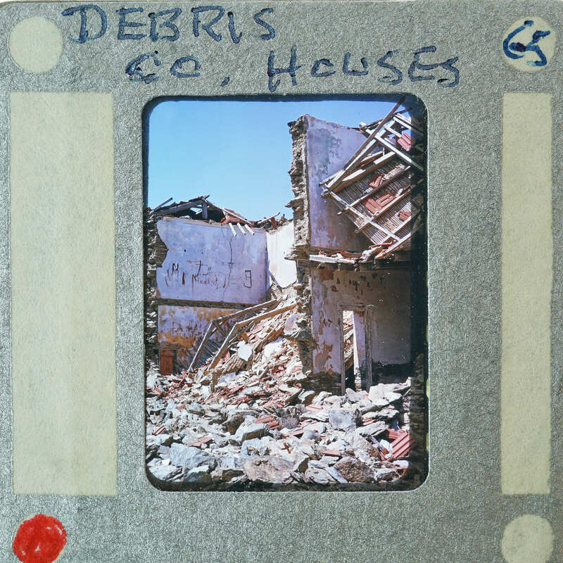A photograph of a damaged building with debris on the ground, framed by an old film strip border.
