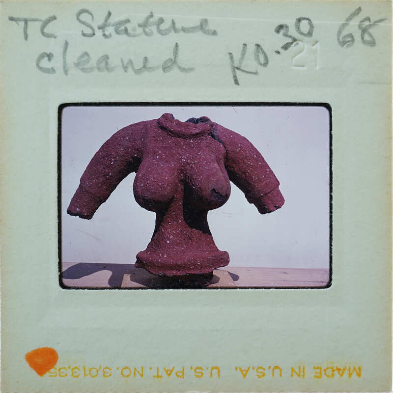 The image features a unique sculpture of a woman's torso made from red beads, displayed on a stand against a white wall.