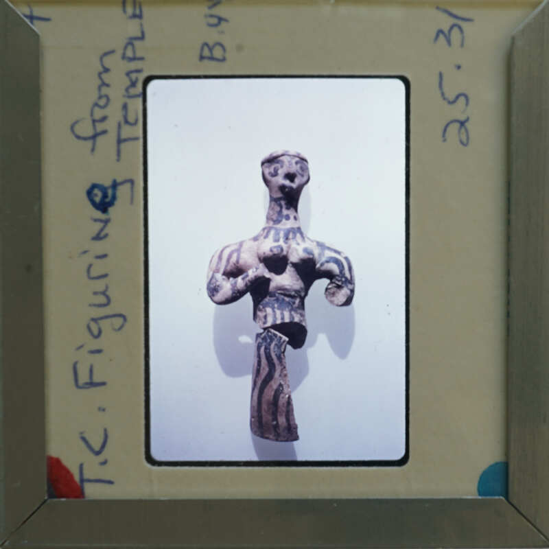 Ancient clay figurine of a humanoid form with detailed markings, displayed on a card within an envelope.