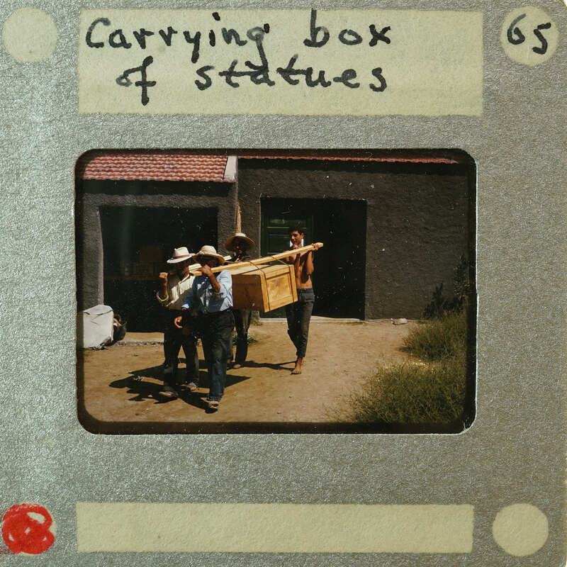 Three men carrying a large box of statues down a street.