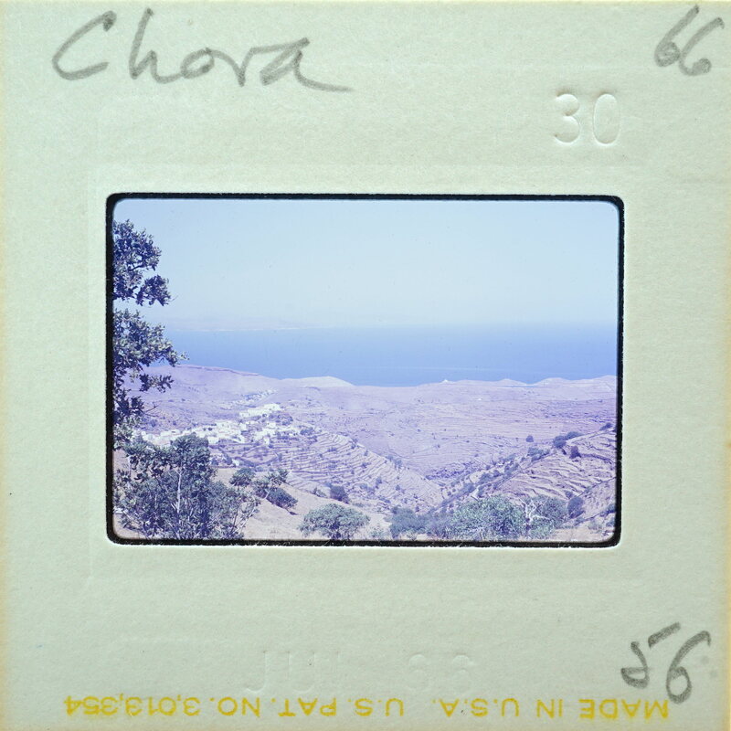 A photograph of a coastal landscape with hills and blue water, enclosed within an old film strip.