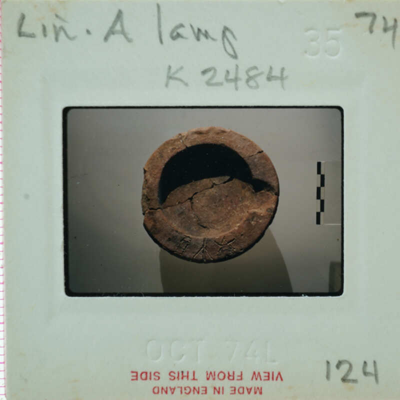 A photograph of a round, weathered object on a white surface with a handwritten label and date.