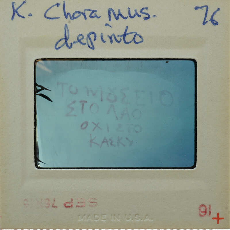 A Polaroid photo with a handwritten message in Greek, displayed on a white card with blue writing and numbers.