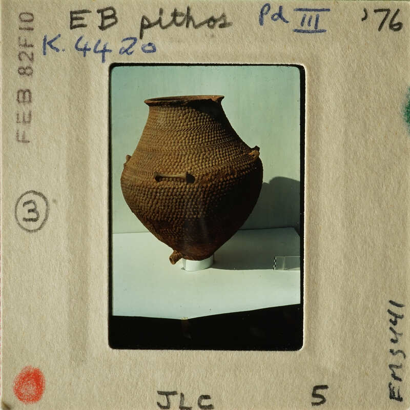 Ancient clay pot with unique texture and shape, displayed on white stand.