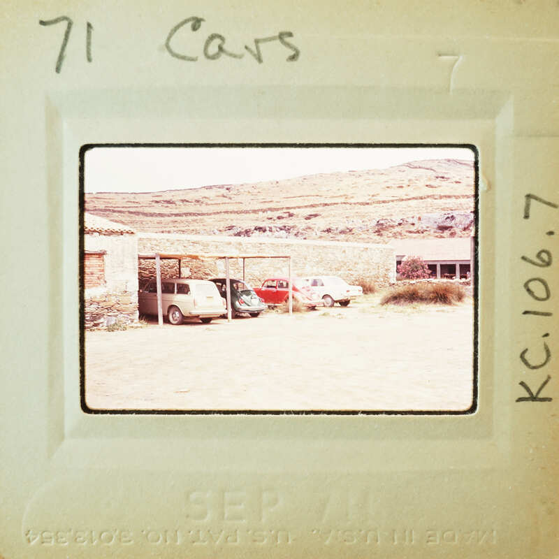 Old photo of a car lot with several parked cars on a dirt ground.