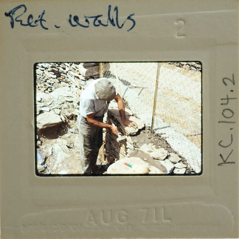 A man working on a stone wall with a hammer and chisel, captured on an old photograph.