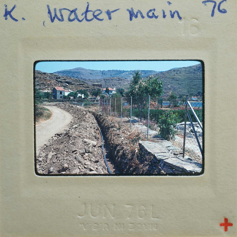 A photograph of a dirt road with mountains and houses in the background, on an old film strip.