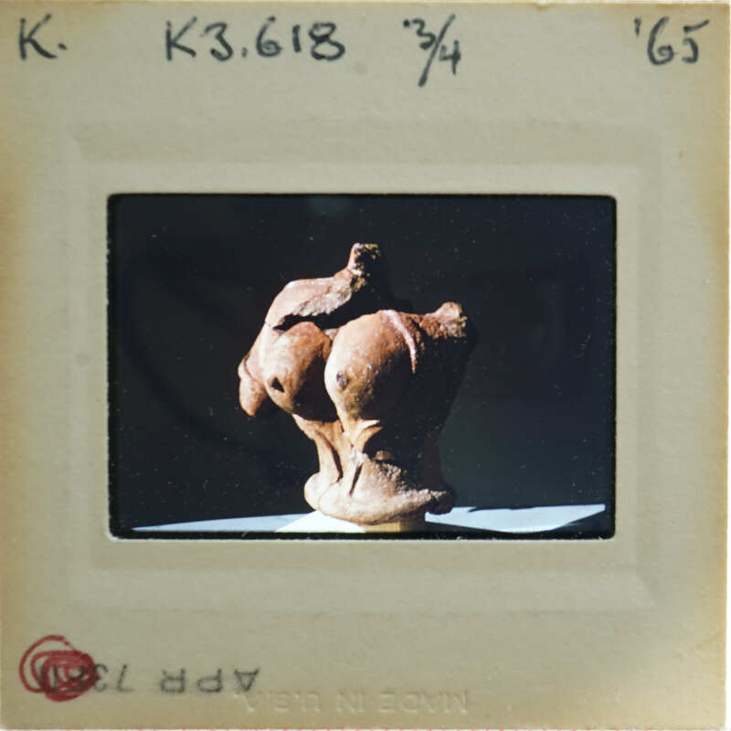 A photograph of a clay figurine torso, displayed on a stand.