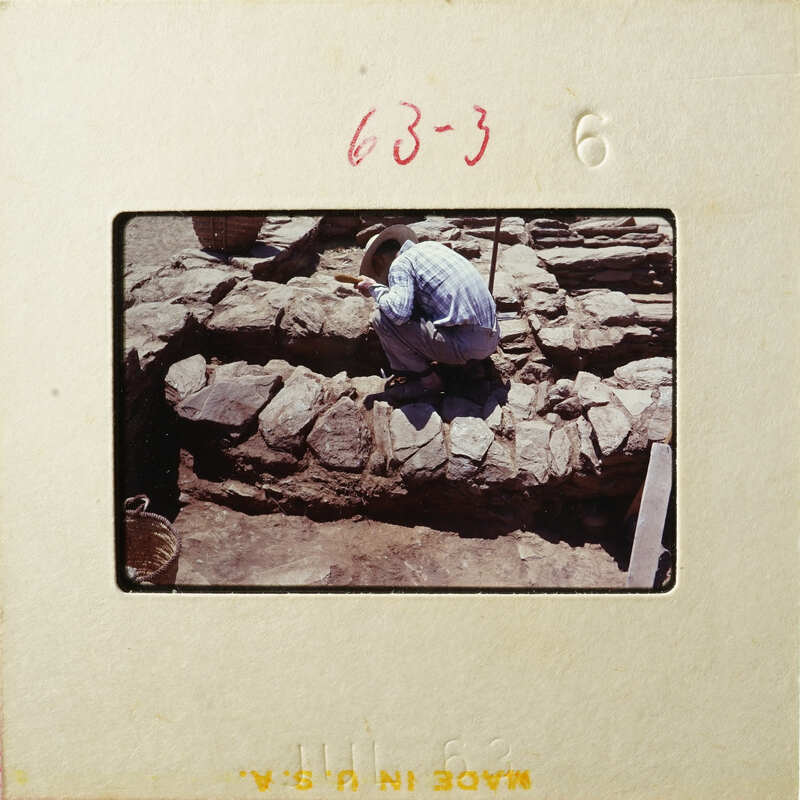 Man kneeling down next to rock wall under construction.