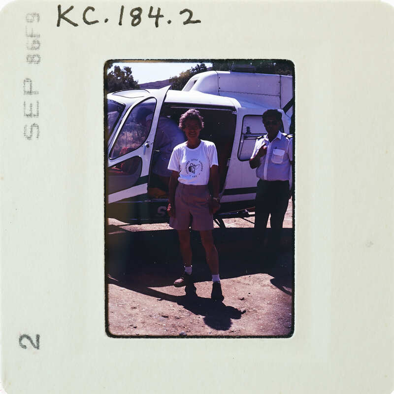 Two people standing next to a helicopter, with one man posing and the other looking on.