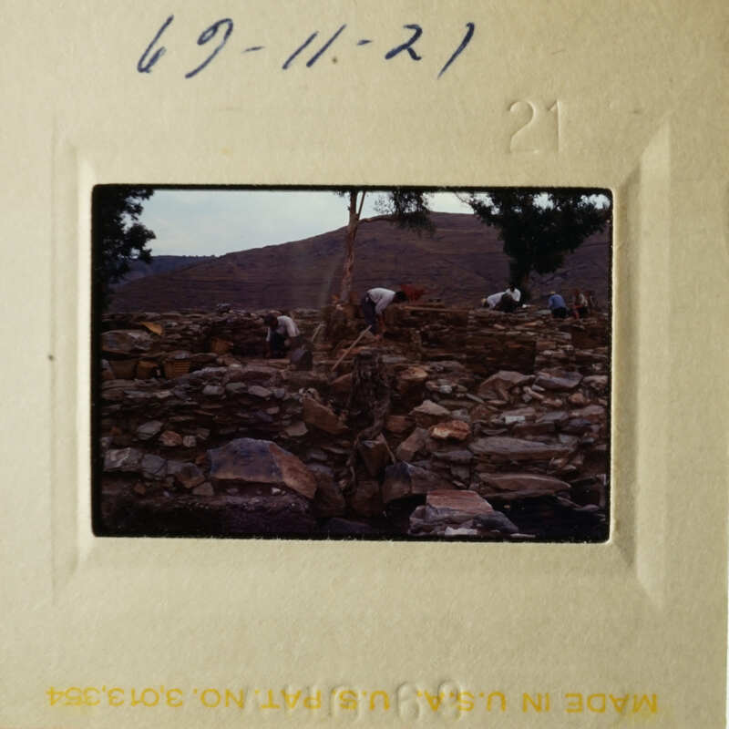 A vintage photograph depicting an archeological site with people working on excavation, featuring stone ruins and a barren landscape under a clear sky.