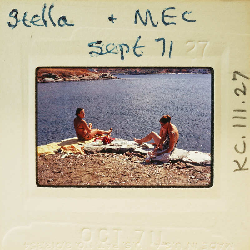 Two people sitting on a rock near water with a handwritten note and date on the photo. Catalog number KC.111.27