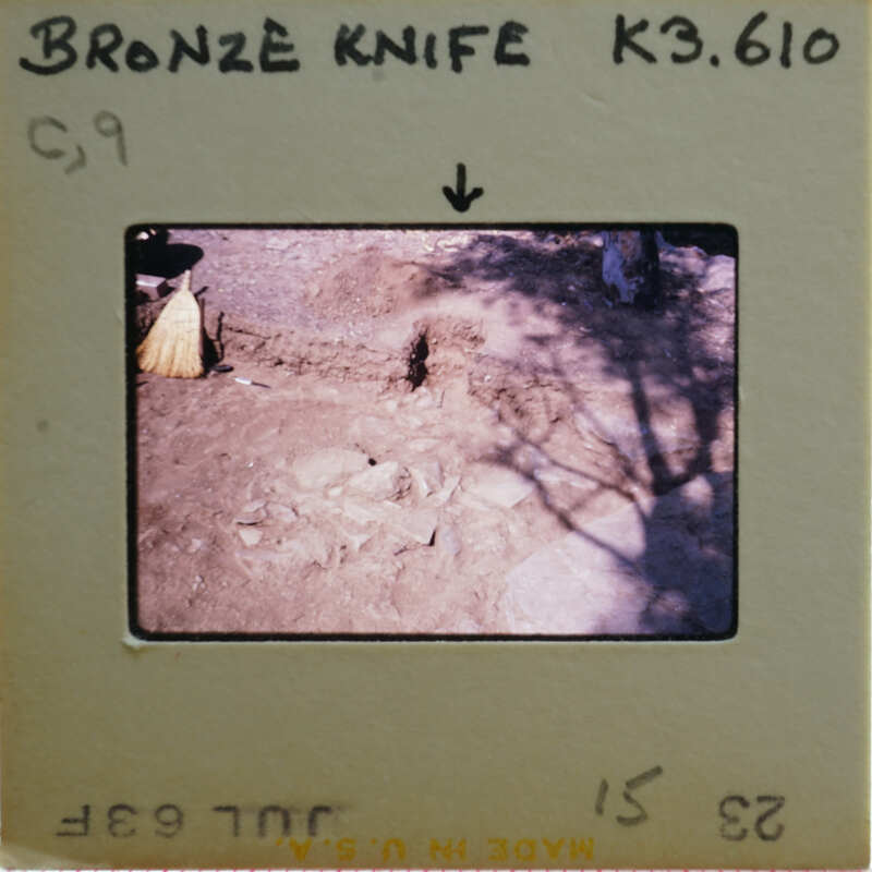 A photograph of a bronze knife on display with an explanatory label and a shadowed background.