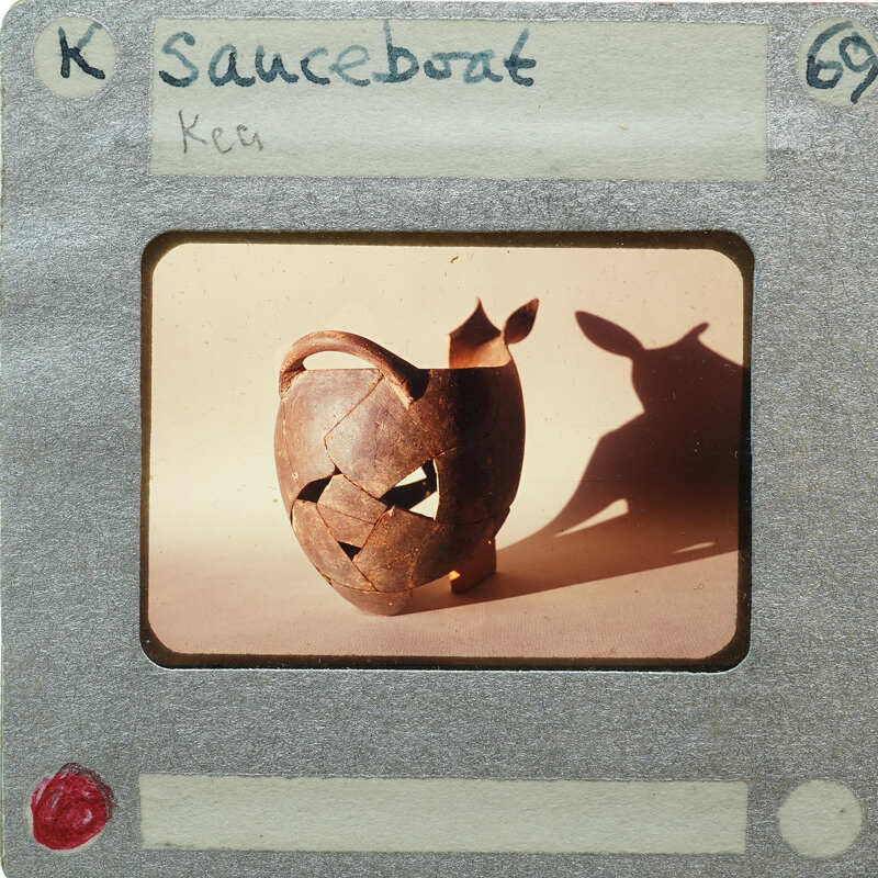 A photograph of a clay pot with an animal shadow on it, placed within a film strip frame labeled "Sauceboat" and numbered 69.