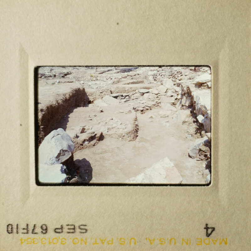 The image shows an archaeological site with stone ruins and rock formations, possibly a historical landmark.