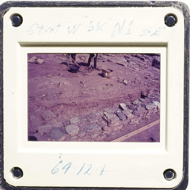 A photograph showing an archaeological site with stone ruins and dirt ground.