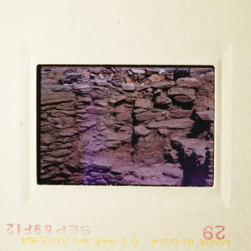 The photo shows an ancient wall made of stone bricks, with moss growing on it, and a small window visible in the upper right corner.