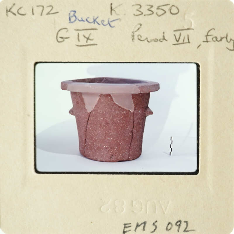 Old clay pot on white surface with handwritten labels and numbers.