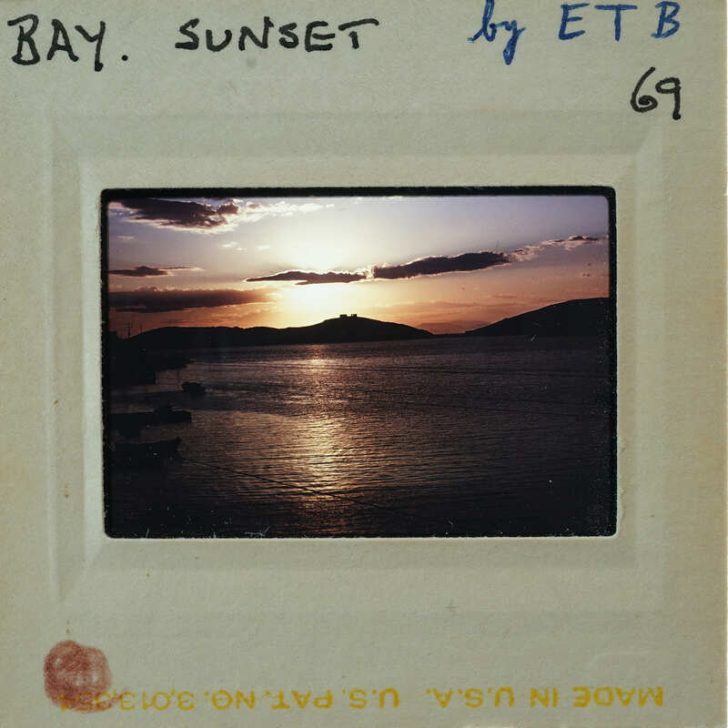 A vintage photograph of a sunset over water with clouds and mountains in the background, enclosed in an old film strip frame.