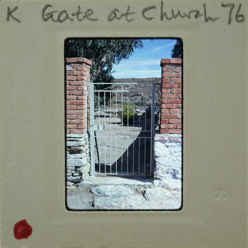 A photograph of a brick archway with a metal gate, featuring an old-fashioned design and surrounded by natural landscape.