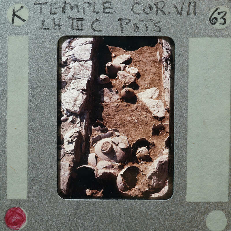 Stone wall on left with pottery on ground in center.