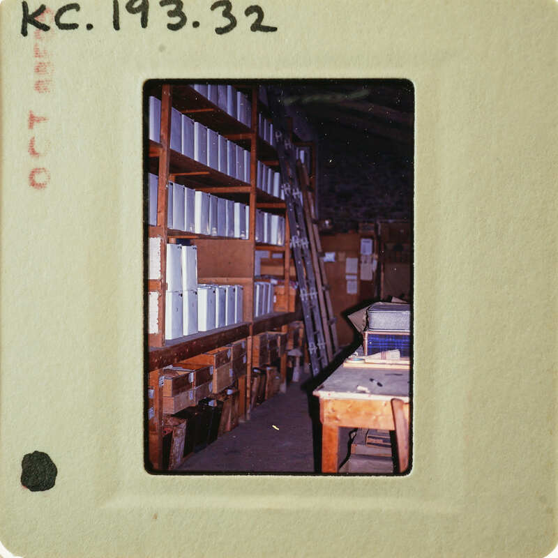 A photograph of a cluttered room with shelves and boxes, taken on film as indicated by the white border around the image.