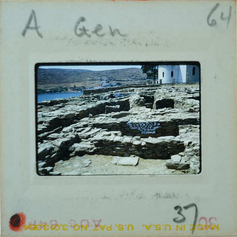 A photograph of ancient ruins with a body of water and mountains in the background.