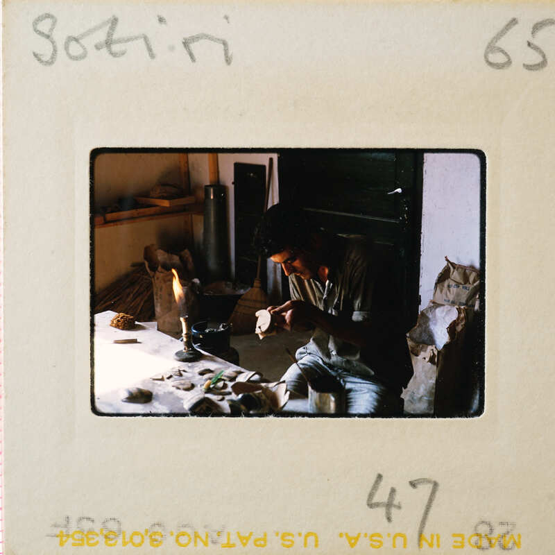 A man sitting at a table with various items, possibly working on something.