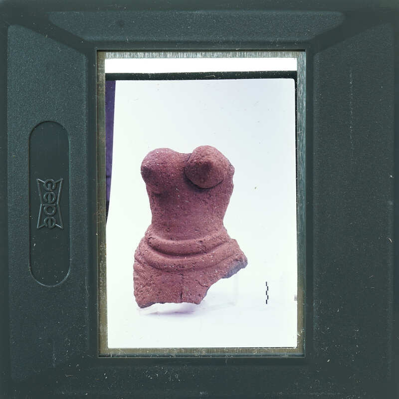 A small, ancient clay figurine displayed on a white background with a camera viewfinder framing the image.
