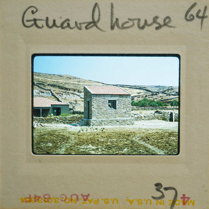 A photograph of a stone structure with a red roof, set against a hilly landscape.