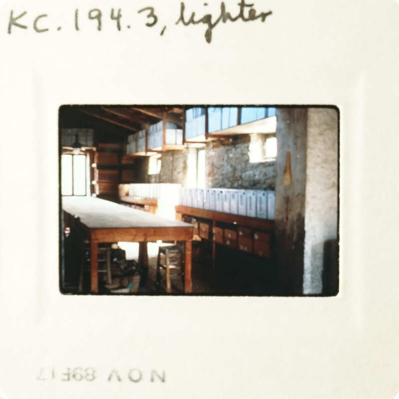An old photo captures an interior space with a table, shelves, and a window.