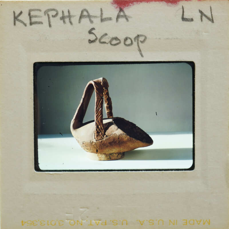 An image of an old, brown clay pot on a white surface with a label that reads "KEPHALA SCOOP".