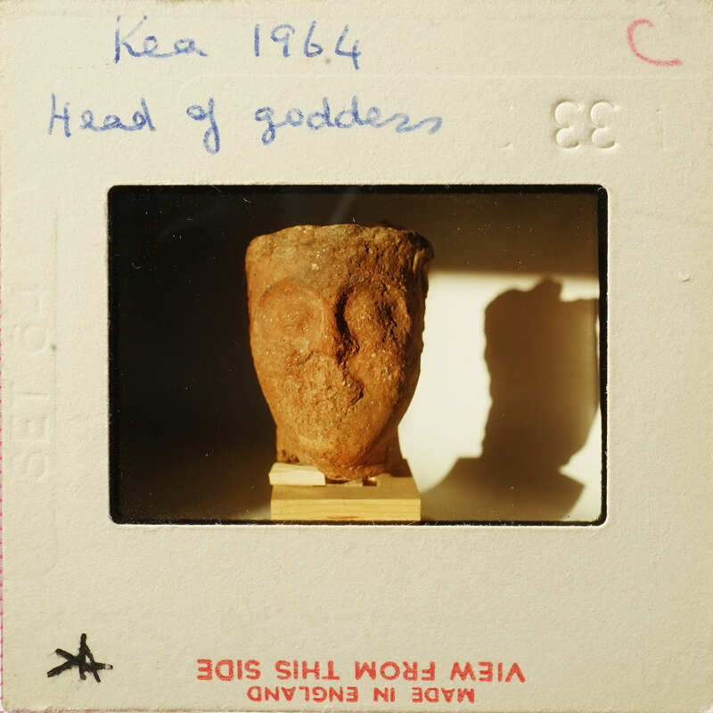 Ancient artifact, possibly a sculpture or figurine, displayed on a stand with visible shadow and light effects.