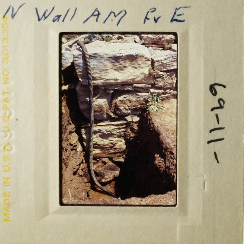 A photograph depicting an old brick wall with a metal pipe running through it, taken from a low angle.