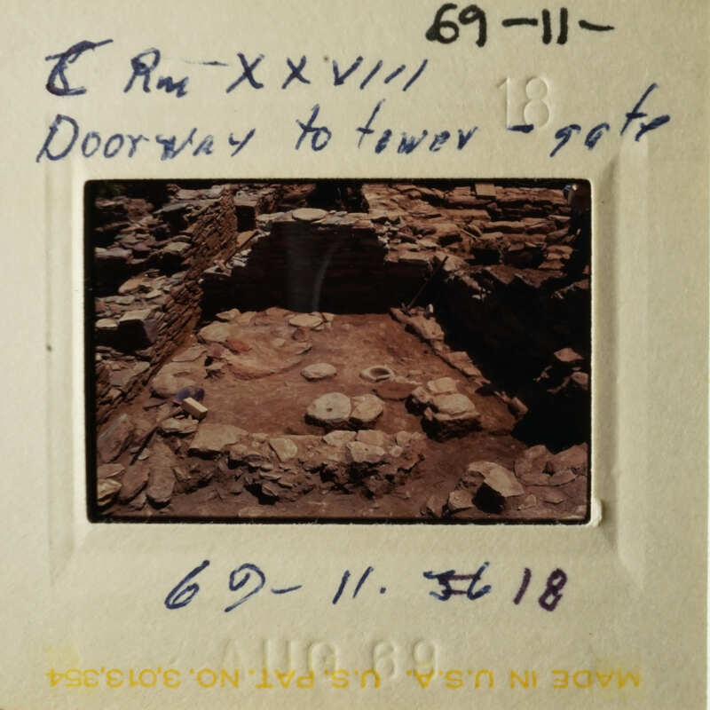 The photo shows an archaeological site with ancient ruins, including stone structures and what appears to be pottery shards scattered about.