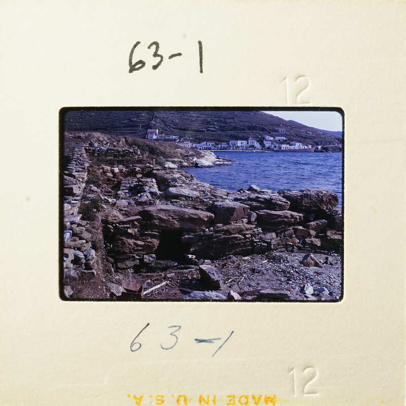 A photograph of a rocky coastline with water and buildings in the background.