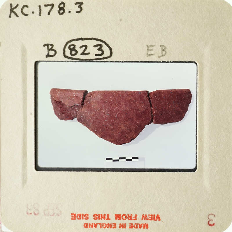 Photograph of a red rock fragment with a label.