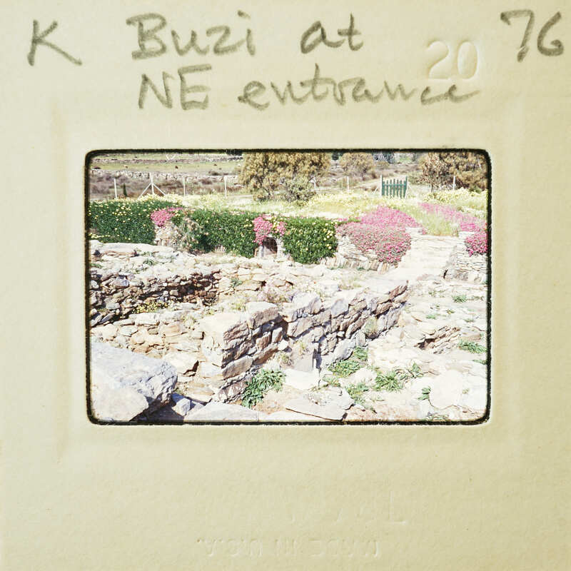 A vintage photograph of a stone structure with greenery and flowers, labeled "K Buzi at NE entrance 20 76".